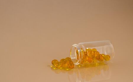 Transparent vial with yellow pills on a glass surface with reflection. Open vial lying on its sideの写真素材
