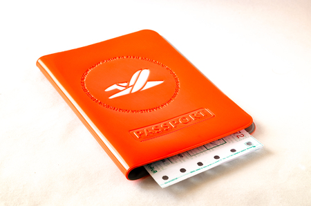 Foreign passport bright orange cover with the back of a perforated plane ticket (train) on a white surface with a shadowのeditorial素材