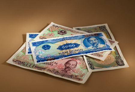 A pile of Vietnamese dongs in denominations of 5000, 2000, 1000 on a beige background with reflections of bright lightのeditorial素材