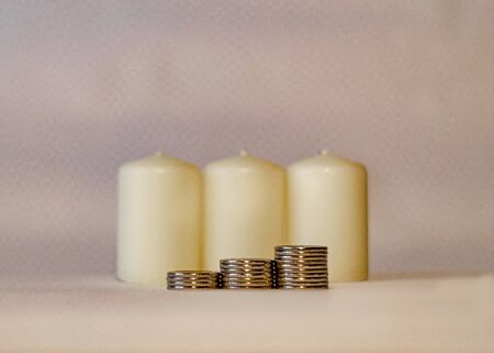 Three piles of coins against three unlit candles. Environmental Protection. Energy savingの写真素材