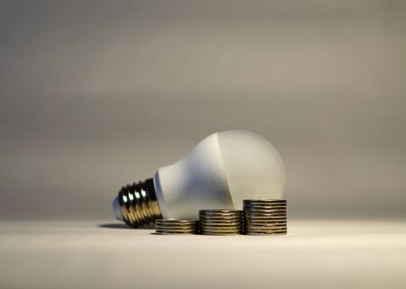 Three piles of coins on the background of the LED light bulb. Symbol of energy saving technology....