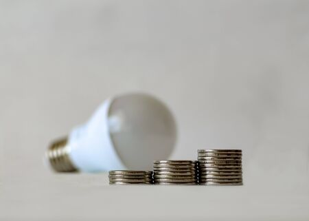 Three piles of coins on the background of the LED light bulb. Energy Saving Symbol