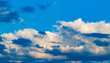 Clouds with shades and shadows against a blue sky, illuminated by the morning sun for half a frame. Patterns of cumulus clouds of different colors.の写真素材