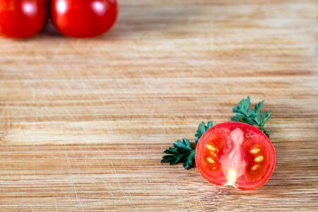 Half sliced tomato on a sprig of parsley and two tomatoes on top in the corner, on a wooden surface