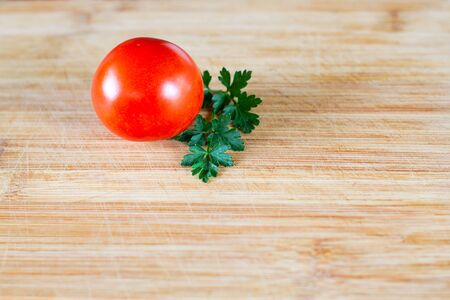 Shiny tomato and a sprig of parsley on a wooden surface at the top of the frame. Top view at an angleの写真素材