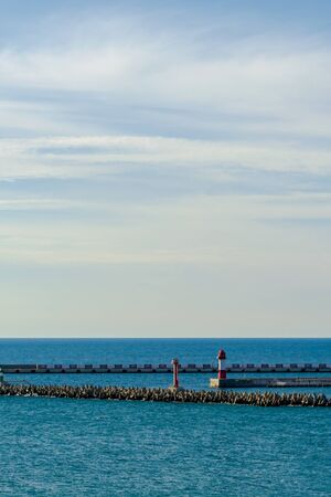 Port infrastructure: ship mooring, red lighthouse at sea and breakwater. Vernical frameの写真素材