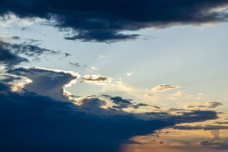 Torn cloud at sunset with shadows. Backlit by the bright yellow sun. Blue sky