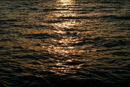 Bright reflection of sunlight on the waves in dark water. Sea at sunset. Evening on the beachの写真素材