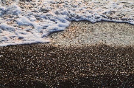 A bubbling wave in motion on wet small pebbles. Glitter of the sun on stones. Clean beach. Ecology conceptの写真素材