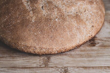 A piece of large round freshly baked whole grain bread on a wooden surface. Crust. Bakery, food concept. Country style. Closeupの写真素材