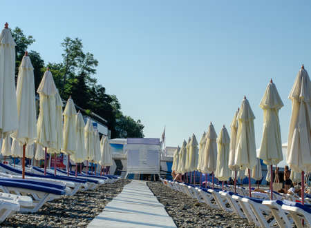 Sochi, Russia - July 20, 2019: A wooden walkway stretching into the distance, between folded beach umbrellas and sun beds. Beach in the morningのeditorial素材