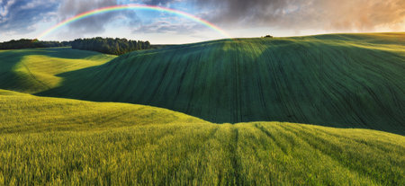 Scenic view of rainbow over green field. dramatic gray sky over a picturesque hilly fieldの写真素材