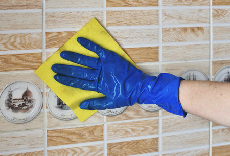 Hand in blue rubber glove cleaning ceramic tile wall with yellow rag.の写真素材