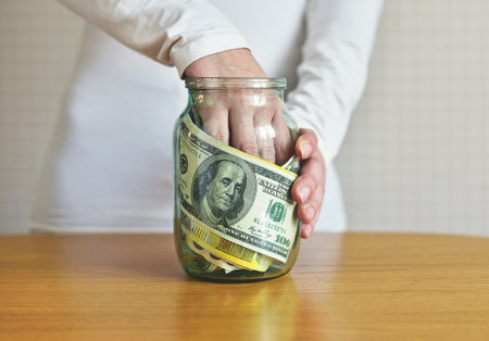 Hands of woman holding money in a glass jar on the tableの写真素材