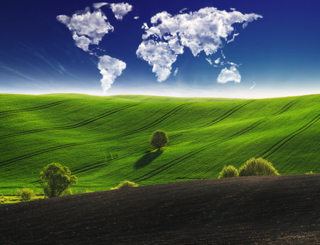 clouds in the form of a world map over a green field. Travel and landscape concept. hilly fieldの写真素材