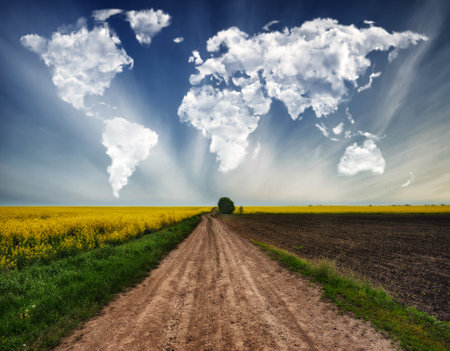 clouds in the form of a map of the world over a hilly field. road in a picturesque field. Travel and landscape conceptの写真素材