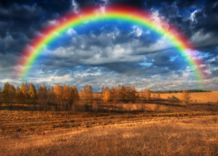 Dramatic sky with a vibrant rainbow over vast, wavy plowed fields on rolling hillsidesの写真素材