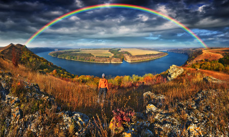 A vibrant rainbow arches over a scenic meadow and river on a clear autumn morningの写真素材