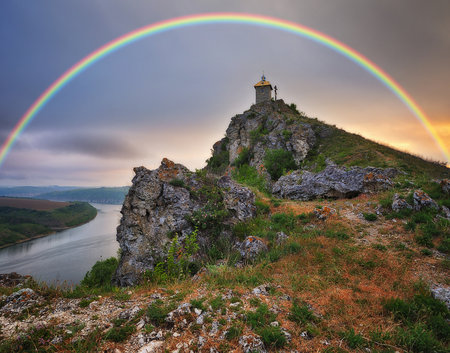 A vibrant rainbow arches over a scenic river on a clear autumn morningの写真素材