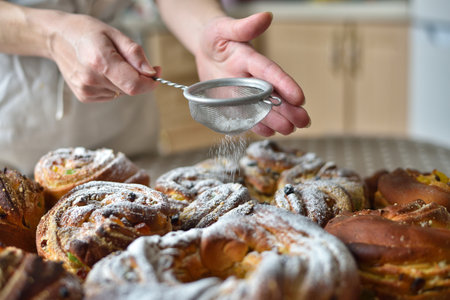 Close-up of a woman's hand using a sieve to dust sweet Easter bread (Paska) with white powdered...
