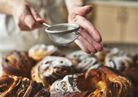 Close-up of a woman's hand using a sieve to dust sweet Easter bread (Paska) with white powdered sugarの写真素材