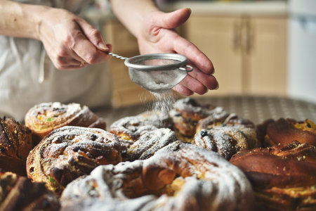 Close-up of a woman's hand using a sieve to dust sweet Easter bread (Paska) with white powdered sugarの写真素材