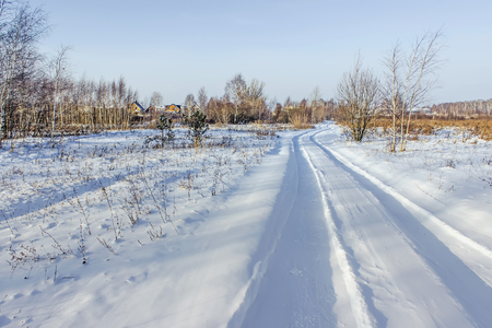 Countryside road through winter field with village on a horizonの写真素材