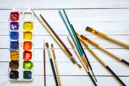Paints and brushes on a white wooden backgroundの写真素材