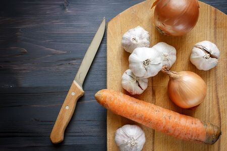 Onion, garlic, carrot and knife on a black wooden backgroundの写真素材