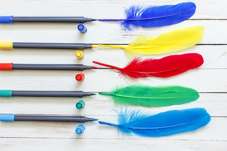 Multicolored markers drawing feathers on a white wooden backgroundの写真素材
