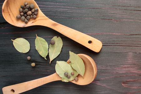 Wooden spoons on a table with leaves of a laurel and grains of pepper. view from aboveの写真素材
