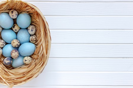 Easter eggs in the basket on a white wooden table. Top view.