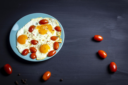 Scrambled eggs with tomato on a plate and dark background