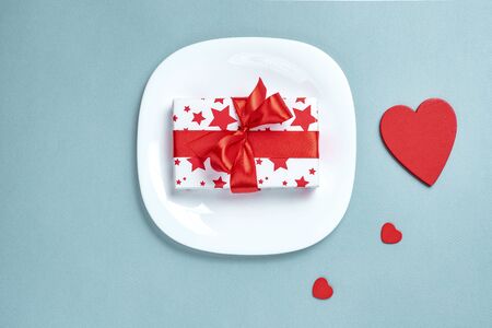 Valentine's day table setting with plate, fork, knife, gift box and red heart, on blue tablecloth...