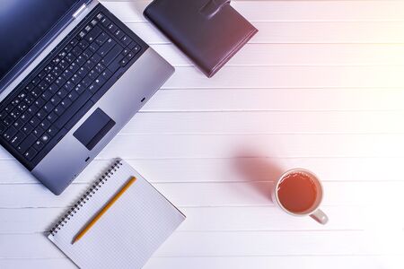 Laptop, notebook with cup of coffee and notepad with pen on white wooden table