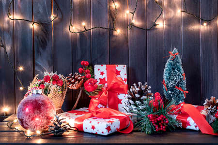 Christmas decoration with pine branches, red ball, and red berries with gifts on wooden background. Flat layの写真素材