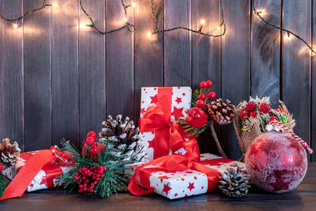 Christmas decoration with pine branches, red ball, and red berries with gifts on wooden background. Flat layの写真素材