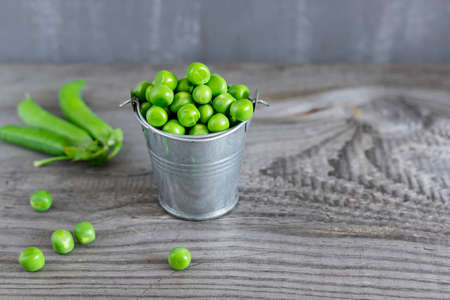 Close-up view of fresh green peas in a small metal bucket on dark wooden table.の写真素材