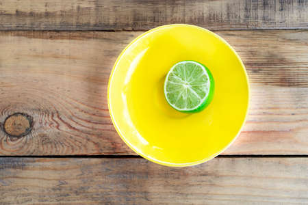 Fresh limes on yellow plate standing on brown wooden table. Healthy organic vegetarian foodの写真素材