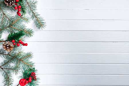 Christmas decoration of fir branches with red berries on a white wooden background. Top view. Flat layの写真素材