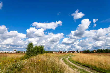 Road to the field and sky with clouds. Autumn and summer landscape.