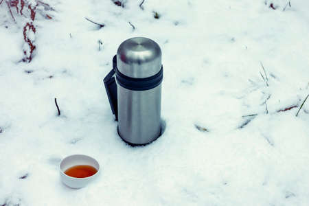 A flask of hot tea in the snow forest, in the open air.の写真素材