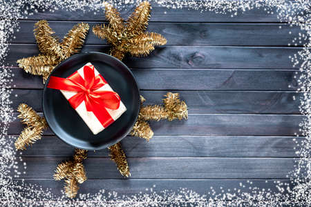 Christmas background concept. Golden spruce branches with gift in black plate on dark wooden background. Space for text. Top view.の写真素材
