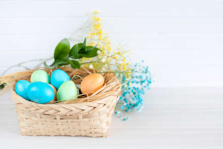 Multicolored Easter eggs lie in a basket that stands on a white wooden tableの写真素材