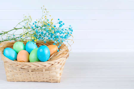 Multicolored Easter eggs lie in a basket that stands on a white wooden tableの写真素材