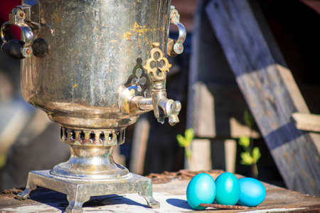 Old samovar with Easter eggs stands on a wooden tableの写真素材