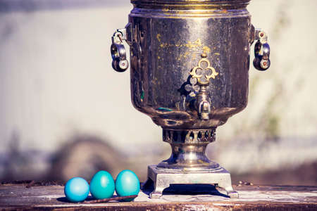 Old samovar with Easter eggs stands on a wooden tableの写真素材