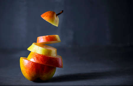 Pear cut into pieces with in the air on a dark background. Concept of the morning breakfast. Close-up with copy spaceの写真素材