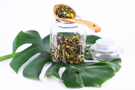 Glass jar with wooden scoop filled with dry herbal tea on white backgroundの写真素材