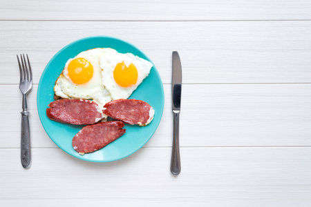 Breakfast of fried smoked sausage and eggs on a blue plate.の写真素材